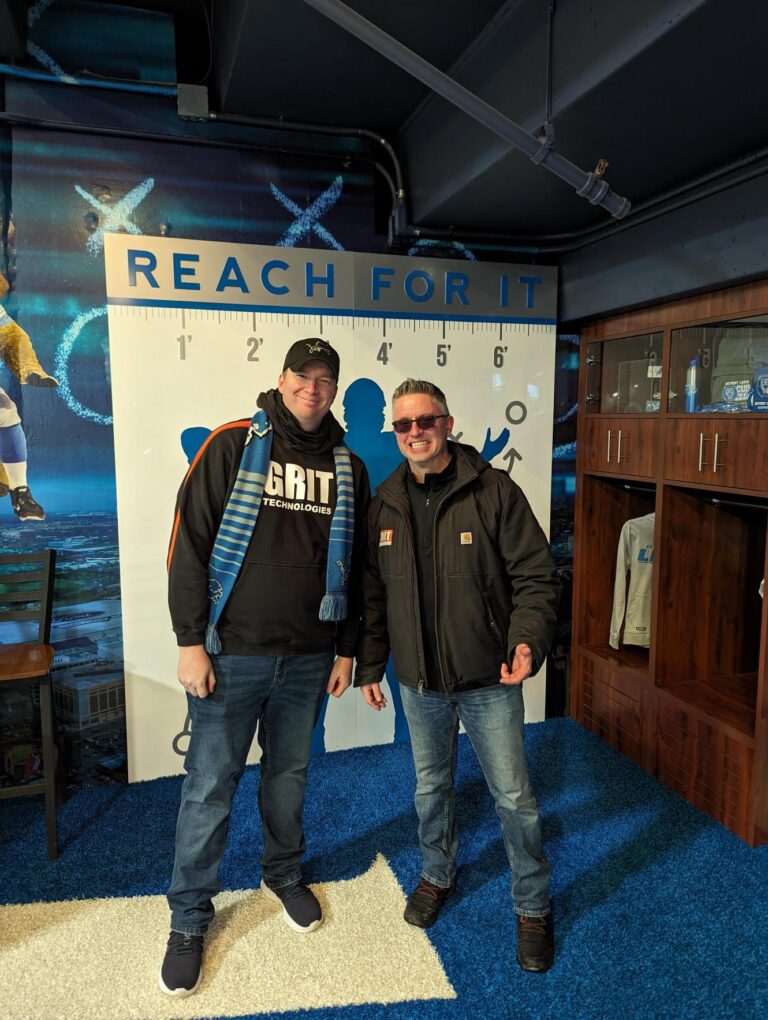 Two GRIT Technologies employees, Tim Boyes and Andrew Hoogerhyde, cheering at the Detroit Lions game.